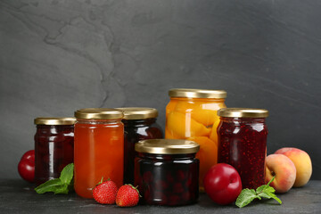 Jars of pickled fruits and jams on grey table