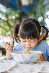 Portrait​ image​ of​ 2-3 years​ old​ of​ baby.​ Happy​ Asian​ child​ girl​ enjoy​ eating​ some​ noodles by​ herself.​ Healthy​ Food​ and​ kid​ concept. Vertical