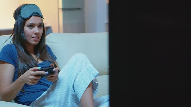 Gamer using joystick playing video games on console sitting on couch in living room. Excited determined woman using controller gamepad keypad playstation gaming and having fun winning electronic game