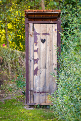 Wooden latrine in the garden with worn-out paint and little wndow in shape of the heart