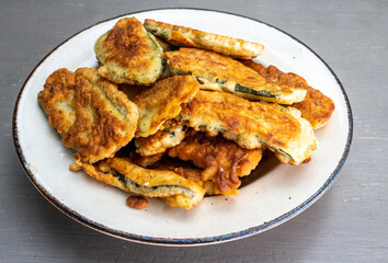 A pile of Courgette fritters in batter in a plate on grey table ,