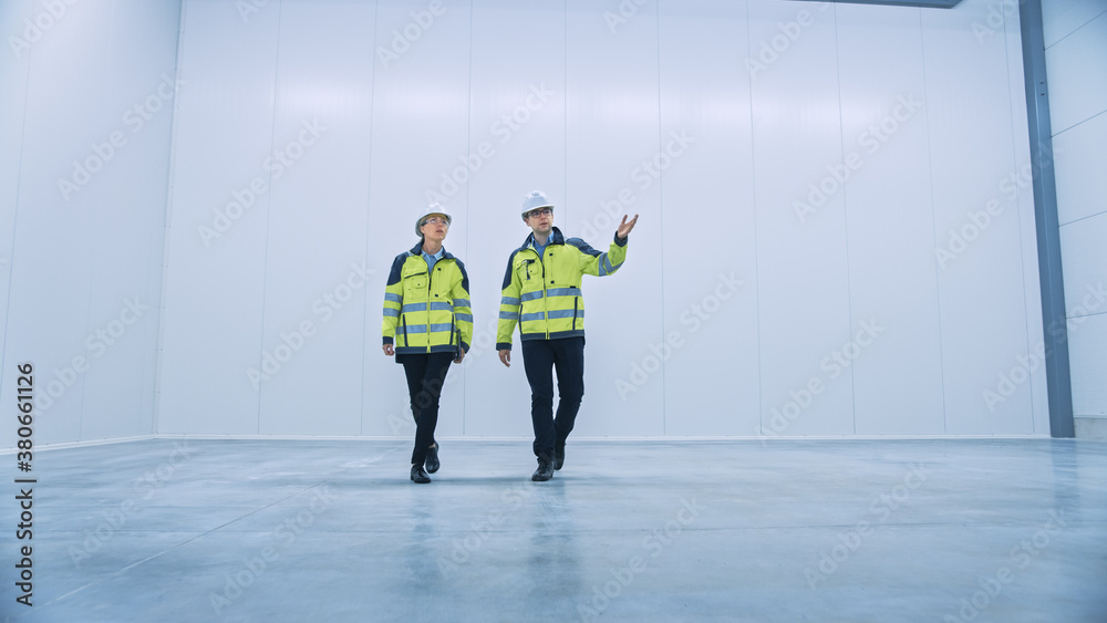 Poster two engineers talking, walking across empty factory floor, inspecting, planning where all the machin