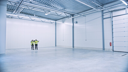 Industry 4.0 Modern Factory: Two Engineers in Empty Warehouse Use Digital Tablet Computer with Augmented Reality Software Visualizing of Manufacturing Plant Room Mapping. Illustrative Mock-up Concept