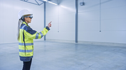 Industry 4.0 Modern Factory: Female Engineer in Empty Warehouse Wearing Augmented Reality Headset...