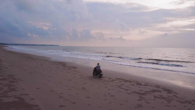 Drone view of a motorcycle riding on the beach side during sunset