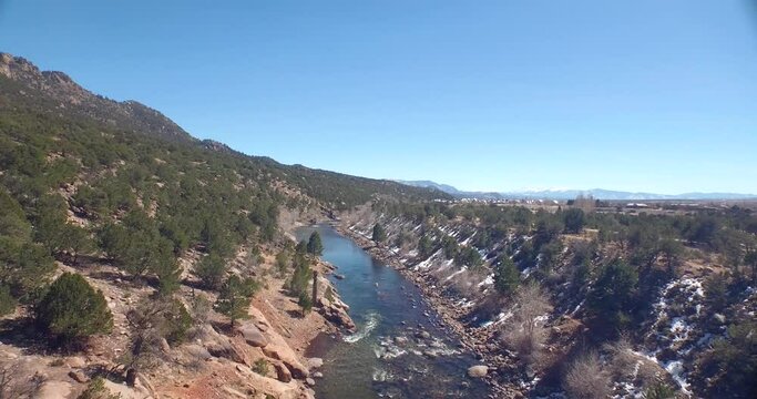 Drone view of a green river in rocky ground with a bit of snow on the ground