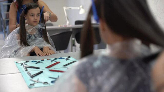 Beautiful little girl looking rubbing her chin choosing air color dye at the beauty salon