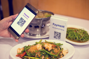 Hand using smart phone to scan QR code on tag with blurry Asian food in restaurants to accepted...