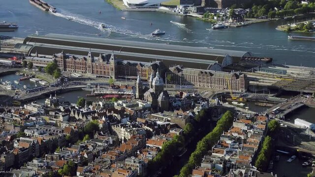 Aerial view of the famous Amsterdam Centraal Station, the largest railway station in Netherlands. Many ferries in the IJ.  Downtown famous buildings.