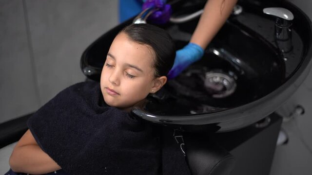 Beautiful little girl looking rubbing her chin choosing air color dye at the beauty salon