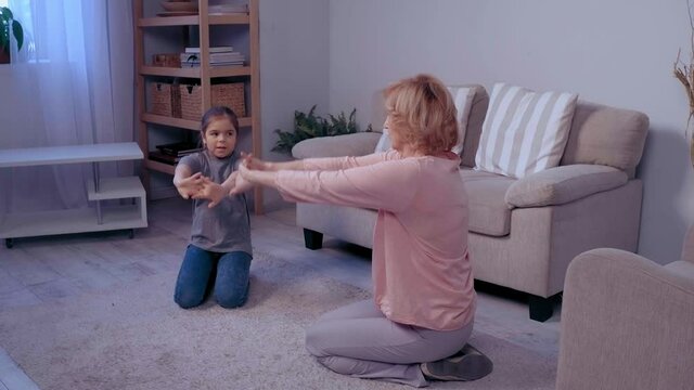 Grandmother and her granddaughter making physical jerks in the room. Indoors activities. Healthy lifestyle. Woman and child . . High quality 4k footage