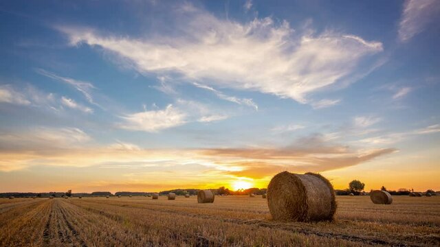 Time lapse video of setting sun over a big field after harvest with bales of straw in autumn