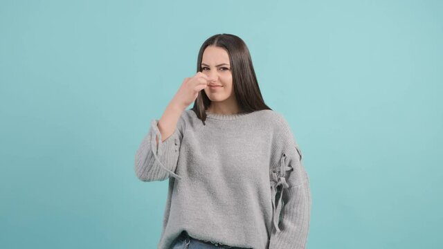 Close up of a caucasian girl that is showing disgust, pinching her nose to avoid bad smell. Negative emotions, nasty feelings.