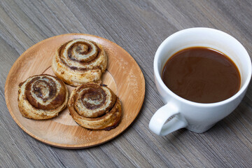 Baked cinnamon burgers. Lie on a plate. Nearby is a cup of coffee.