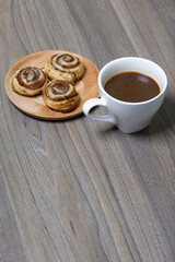 Baked cinnamon burgers. Lie on a plate. Nearby is a cup of coffee.