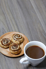 Baked cinnamon burgers. Lie on a plate. Nearby is a cup of coffee.