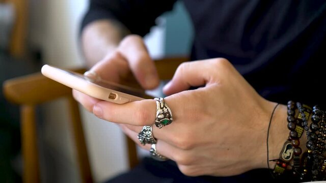 Close-up of bejeweled male hands typing on a smartphone