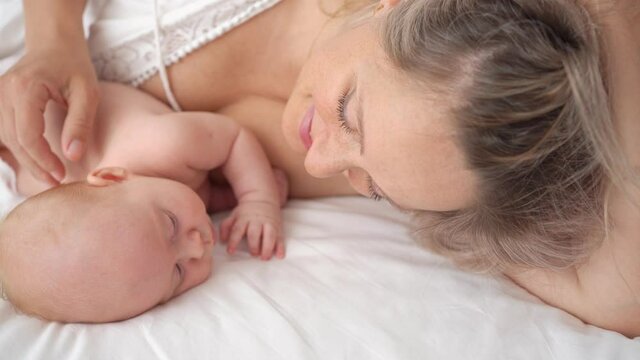 mom lies with baby in bed kisses hands. concept of maternal love, newborn care.