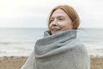 Young adult female wrapped in towel on beach in winter