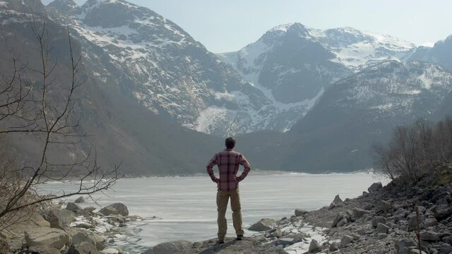 A Hiker Enjoys an Amazing View of a Frozen Lake and Bondhusdalen Glacier in the Mountains of Norway