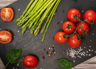 tomatoes on a black board with asparagus with spinach and spices top view