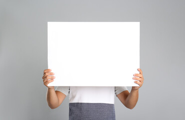 Man holding white blank poster on grey background. Mockup for design