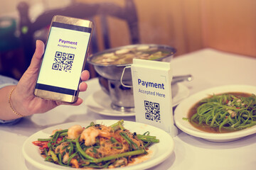 Hand using smart phone to scan QR code on tag with blurry Asian food in restaurants to accepted...