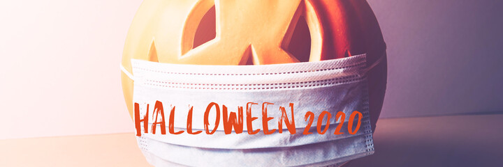 Halloween 2020 text. New Normal and New reality concept. Orange Pumpkin or Halloween Jack o Lantern in medical protective mask, halloween and covid-19 concept, banner size