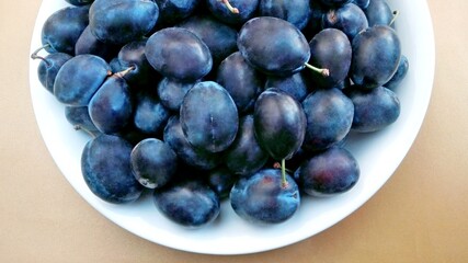 Juicy ripe sweet plums (prunus domestica) closeup on white plate. Organic tasty purple plums on brown background. Plums for diet, jam, pie, juice, dry - harvest from farm. Nutrition, eat plum concept