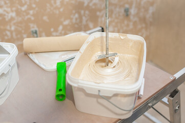 The construction mixer mixes the golden beige paint in the container.