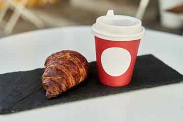 Red cup with coffee and a croissant on a table in a cafe. Morning breakfast. High-quality photo