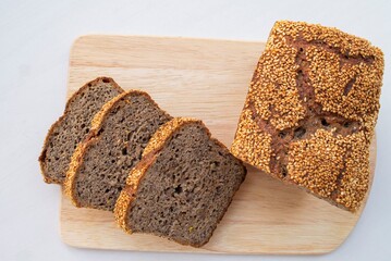 Composition in natural daylight. Homemade whole grain rye bread, with sesame seeds, sliced on a wooden board. View from above