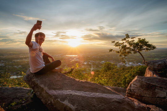 man sitting relax and use cellphone take picture on top of a moutain watching the sunset
