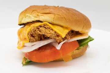 Delicious Fried Chicken Sandwich with Cheese Tomatoes Lettuce and Onions on a White Plate
