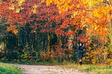 Woman in a hat with a beautiful figure enjoys the nature. Autumn park at a daytime. Yellow and orange colors.