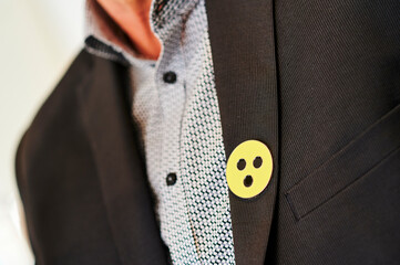 Mann trägt ein gelbes rundes Abzeichen mit drei schwarzen Punkten als Zeichen für eine Sehbehinderung am grauen Sacko - obrazy, fototapety, plakaty