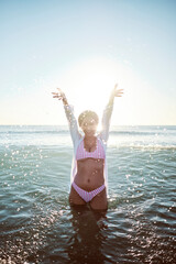 Sexy beautiful latin girl having a bath and playing with the water on a deserted beach wearing a pink bikini and pink sunglasses.
