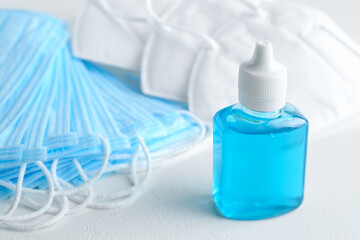 Hand sanitizer and respiratory masks on white table. Protective essentials during COVID-19 pandemic