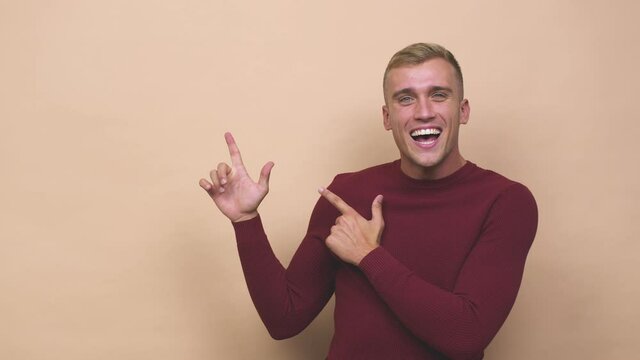 Young caucasian man pointing with forefingers to a copy space, expressing excitement and desire