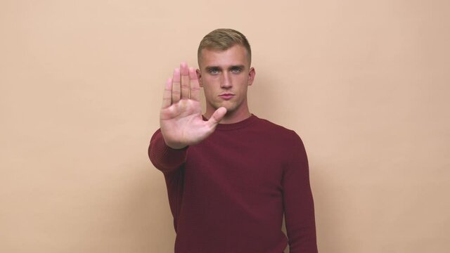 Young caucasian man standing with outstretched hand showing stop sign, preventing you