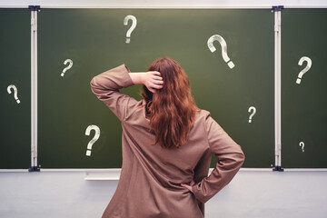 Woman teacher stands pensively against the background of a school blackboard with question marks © Андрей Журавлев