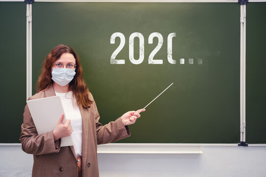 Teacher in a medical mask at the blackboard with an indeterminate year of the end of quarantine. Concept of problems at school during the coronavirus epidemic