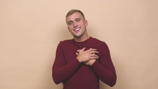 Young caucasian man has friendly expression, pressing palm to chest love concept