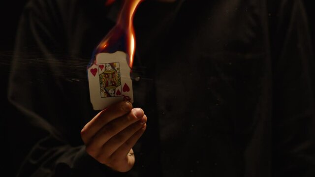 Close-up of a Magician Hand Performing Card Trick . Burning queen card on black Background with smoke . Card Mechanic holding flaming card in hand . Shot on ARRI Alexa cinema camera in Slow Motion