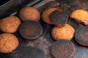 Burnt cookies. Burnt, burnt oatmeal cookies lie on a black baking sheet.