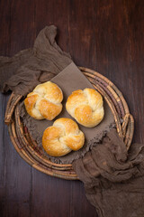 Three Homemade Kaiser Rolls Topped with Sesame Seeds in an Old Woven Bread Basket on a Wood Table