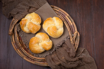Three Homemade Kaiser Rolls Topped with Sesame Seeds in an Old Woven Bread Basket on a Wood Table