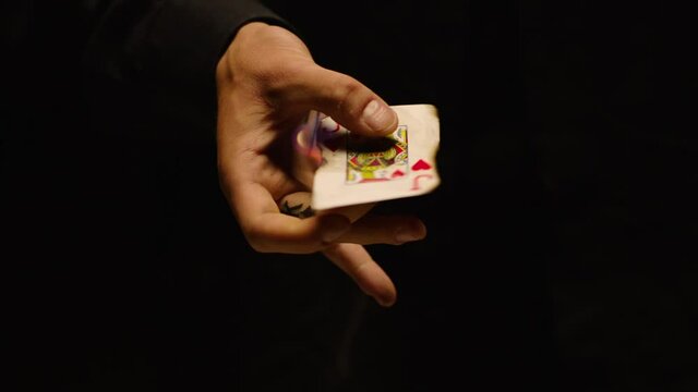 Close-up of a Magician Hand Performing Card Trick . Burning card on black Background with smoke . Card Mechanic rotating flaming card in hand . Shot on ARRI Alexa cinema camera in Slow Motion