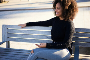 Smiling woman sitting on bench with smartphone