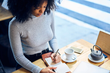 Crop woman writing in notebook at cafe table